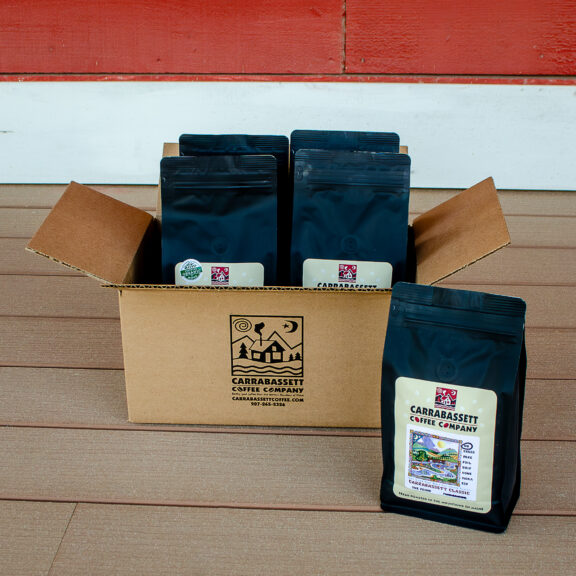 A photograph of a Carrabassett Coffee mailing box (with our logo on it) with carrabassett coffee's one-pound mail order bags inside and one bag od Carrabassett Classic in front.